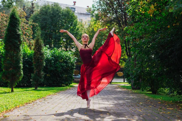 Woman ballerina in red ballet dress dancing in pointe shoes in autumn park.