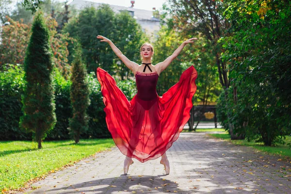 Bailarina de mujer en vestido de ballet rojo bailando en zapatos puntiagudos en el parque de otoño . — Foto de Stock