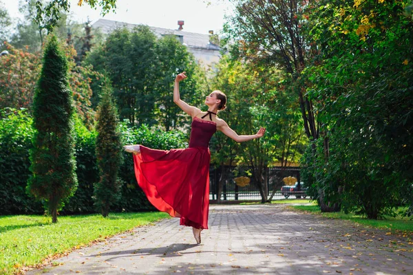 Vrouw ballerina in rood ballet jurk dansen in pointe schoenen in de herfst park. — Stockfoto