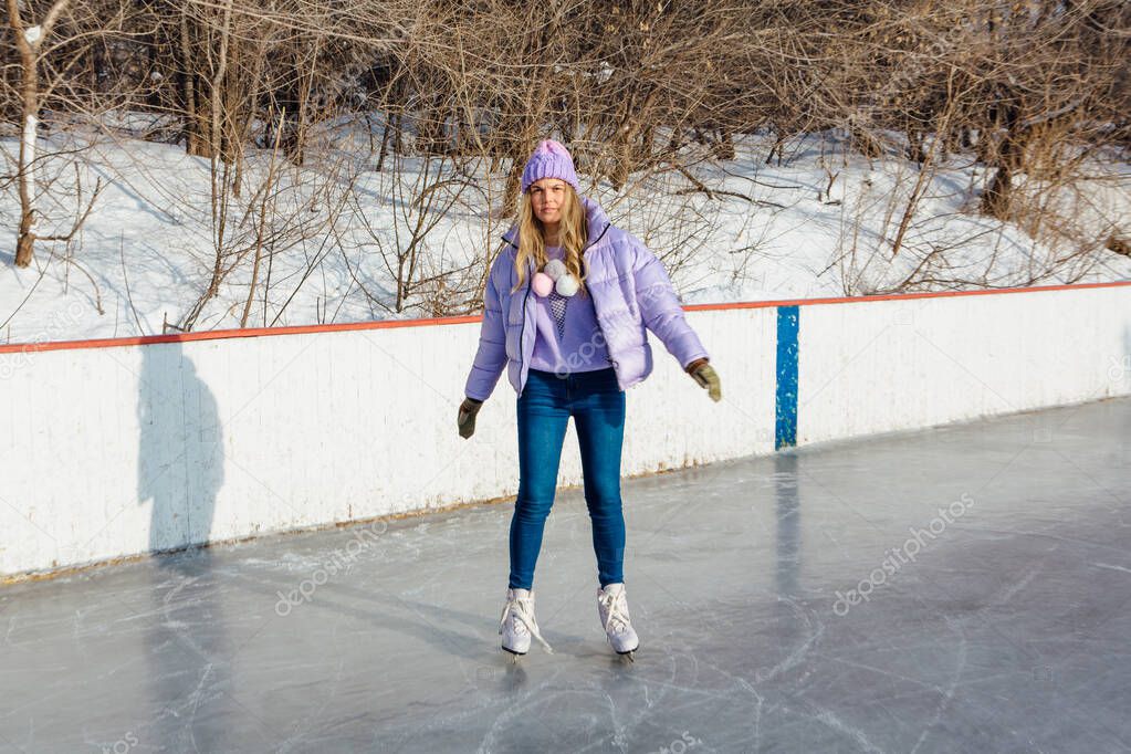 Lovely young woman riding ice skates on the ice rink.