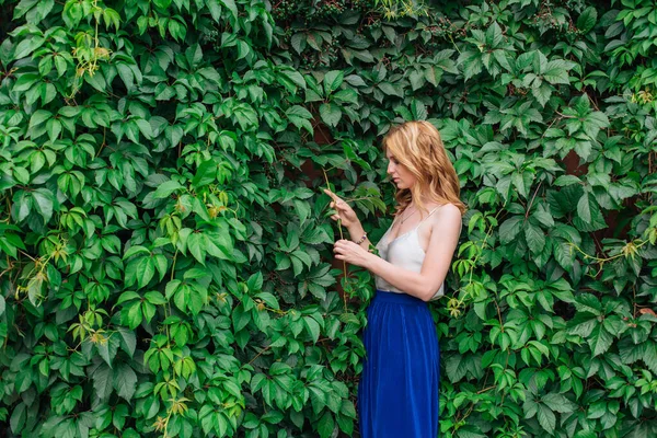 Retrato de una joven mujer hermosa, de pie junto a la pared de hojas de uva silvestre . — Foto de Stock