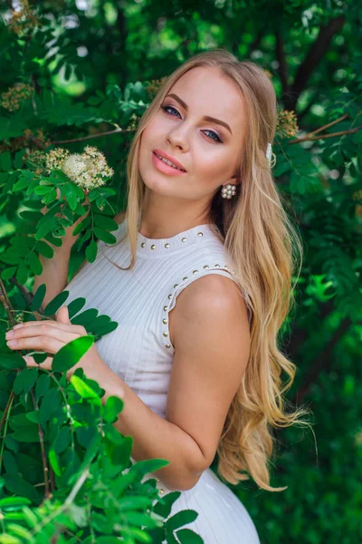 Portret van een charmante blonde vrouw het dragen van mooie witte jurk staande naast Rowan tree. — Stockfoto