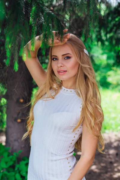Portret uroczej blond kobieta ubrana w piękną białą sukienkę stojący pod futro drzewo. — Zdjęcie stockowe