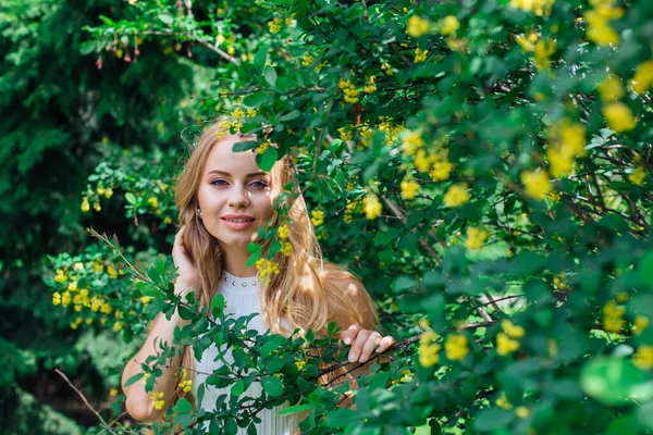 Retrato de cerca de una encantadora mujer rubia con hermoso vestido blanco de pie junto al arbusto de arándanos . — Foto de Stock