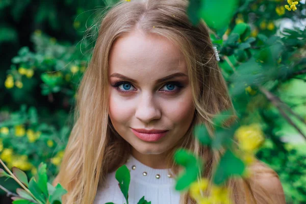 Ritratto ravvicinato di una affascinante donna bionda che indossa un bellissimo vestito bianco in piedi accanto al cespuglio di crespino . — Foto Stock