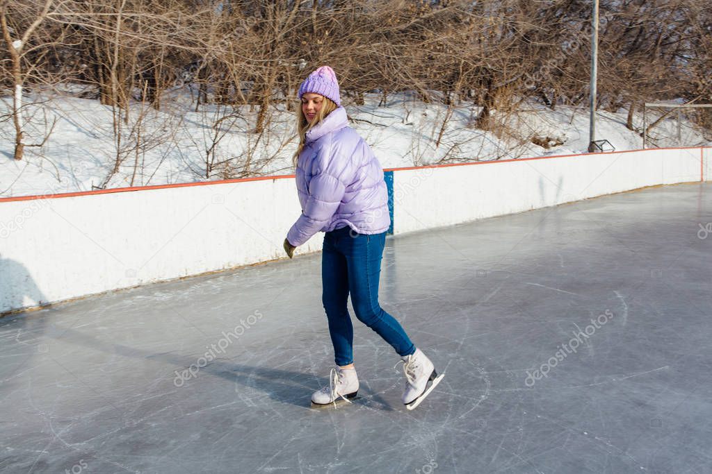 Lovely young woman riding ice skates on the ice rink.