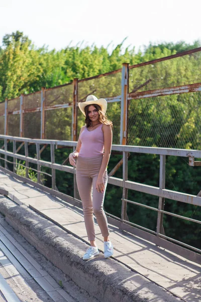 Mulher bonita usando chapéu de cowboy posando na velha ponte enferrujada durante o pôr do sol . — Fotografia de Stock