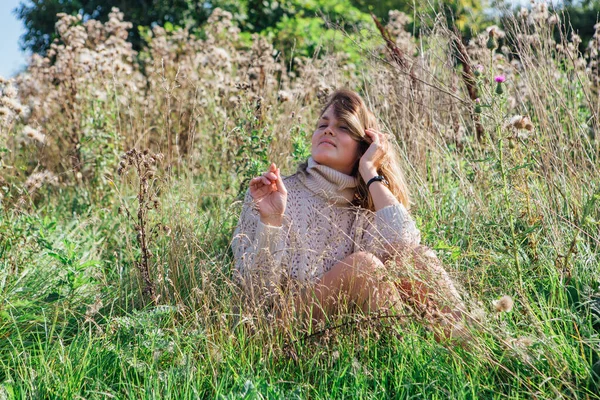 Happy young beautiful woman in sweater and underpants sitting with bare foot in a field of dry agrimony — Stock Photo, Image