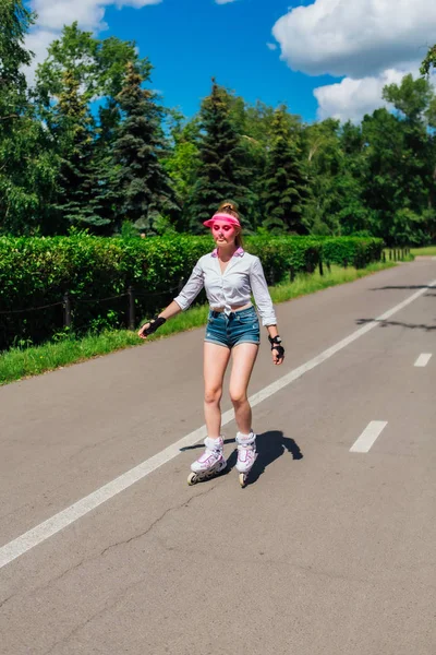 Портрет емоційної дівчини в рожевому ковпачку і захисні рукавички для роликових лопатей і катання на скейтборді на роликових лопатях на дорозі . — стокове фото