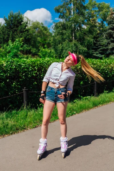 Retrato de una chica emocional en una visera de gorra rosa y guantes protectores para patines y patinetas montadas en patines en la carretera . — Foto de Stock