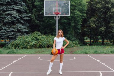 Güzel genç kız beyaz tişört, şort ve spor ayakkabısı, giyinmiş bir basketbol sahası üzerinde bir top ile çalış.
