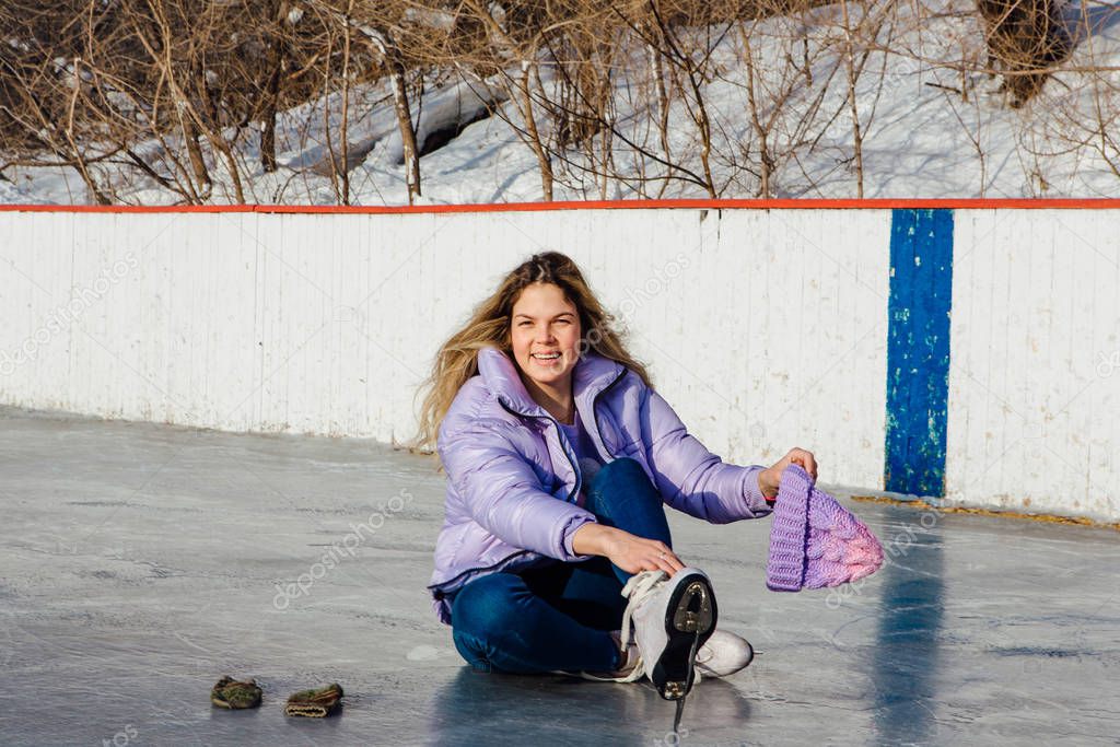 Lovely young woman sitting on ice ring and tieing shoelaces