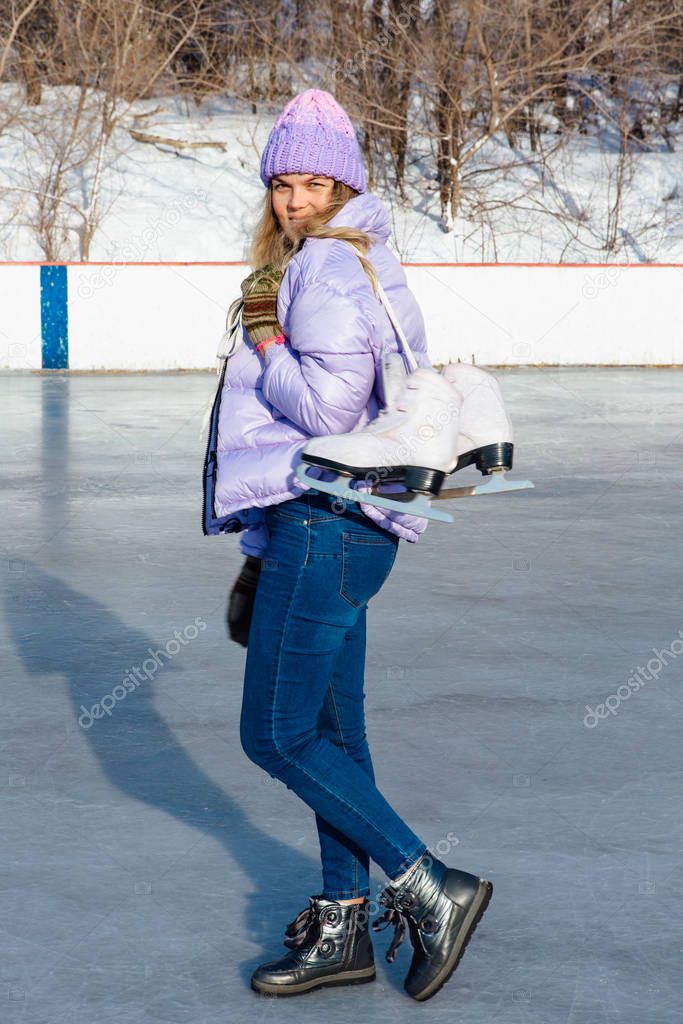 Lovely young woman with ice skates hanging on neck on the ice rink.