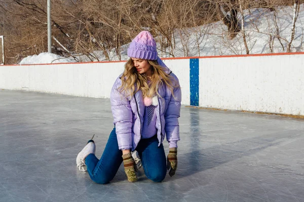 Preciosa joven sentada en la pista de hielo con patines de hielo en los pies . — Foto de Stock