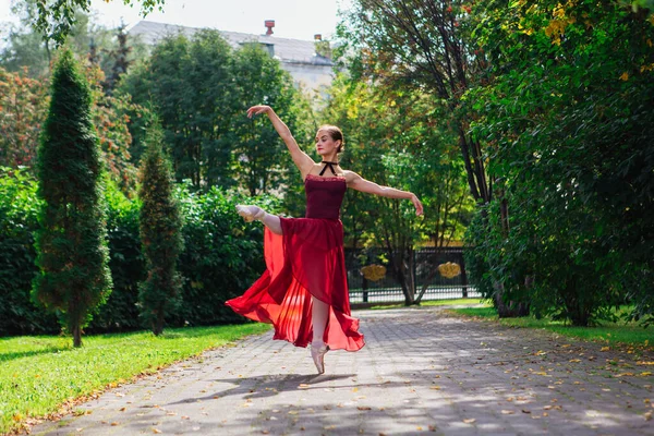 Woman ballerina in red ballet dress dancing in pointe shoes in autumn park.