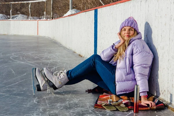 Belle jeune femme relaxante après avoir chevauché des patins à glace et bu une boisson chaude du termo pot sur la patinoire . — Photo