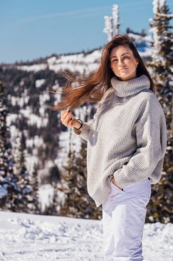 Kışın karlı dağ manzarasında mavi gözlü ve yüzünde çiller olan güzel esmer bir kadının portresi. Kışın açık havada güzel bir kız.