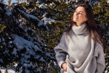 Kışın karlı dağ manzarasında mavi gözlü ve yüzünde çiller olan güzel esmer bir kadının portresi. Kışın güzel bir kız kürk ağacının yanında duruyor..