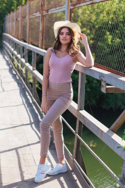 Gün batımında eski paslı köprüde poz veren kovboy şapkası takan güzel genç bir kadın..