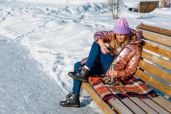 Joven chica rubia hermosa se sienta en un banco en el parque de invierno — Foto de Stock