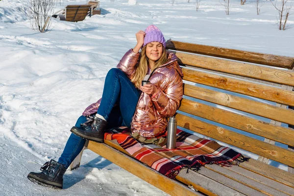 Giovane bella ragazza bionda si siede su una panchina nel parco invernale — Foto Stock