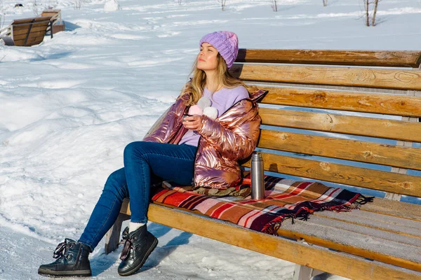 Menina loira bonita jovem senta-se em um banco no parque de inverno — Fotografia de Stock