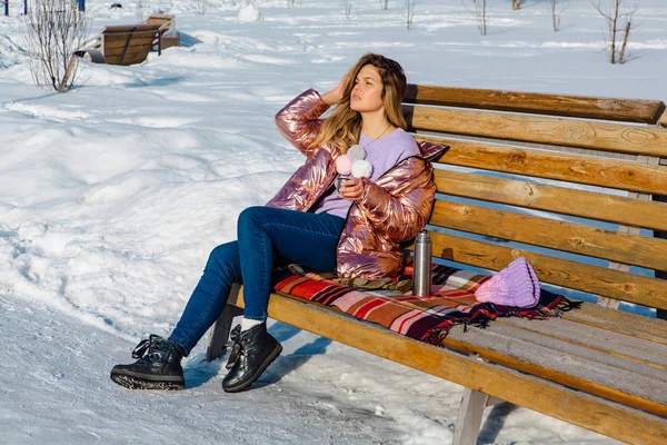 Menina loira bonita jovem senta-se em um banco no parque de inverno — Fotografia de Stock
