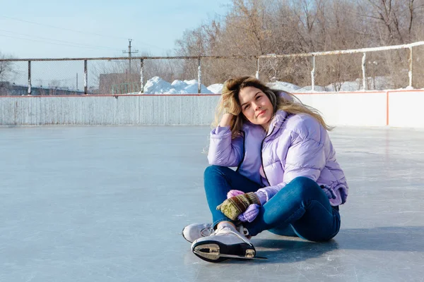 Belle jeune femme assise sur la patinoire avec des patins à glace sur les pieds . — Photo