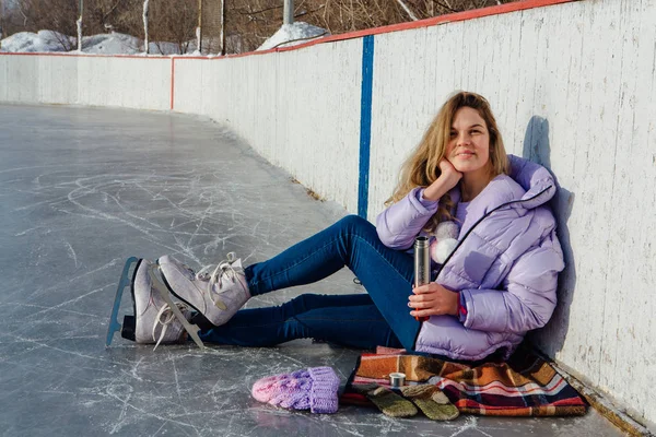 Krásná mladá žena relaxační po jízdě na bruslích a pití teplého nápoje z termo hrnce na kluzišti. — Stock fotografie