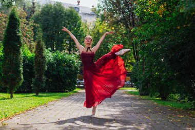 Sonbahar parkında kırmızı bale elbisesiyle dans eden kadın balerin..