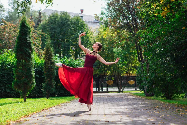 Ballerina donna in abito da balletto rosso che balla in scarpe da punta nel parco autunnale . — Foto Stock