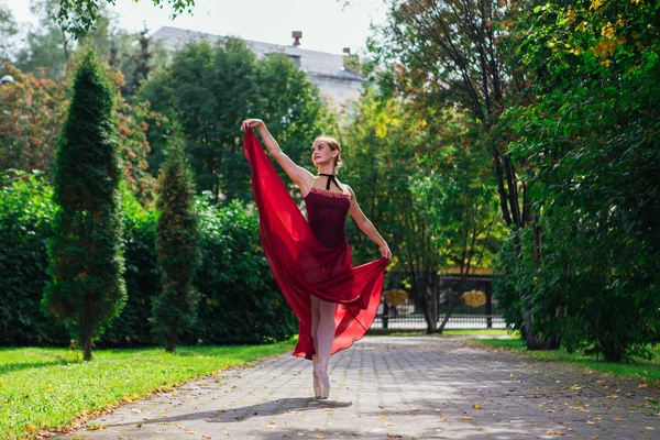 Bailarina de mujer en vestido de ballet rojo bailando en zapatos puntiagudos en el parque de otoño . —  Fotos de Stock