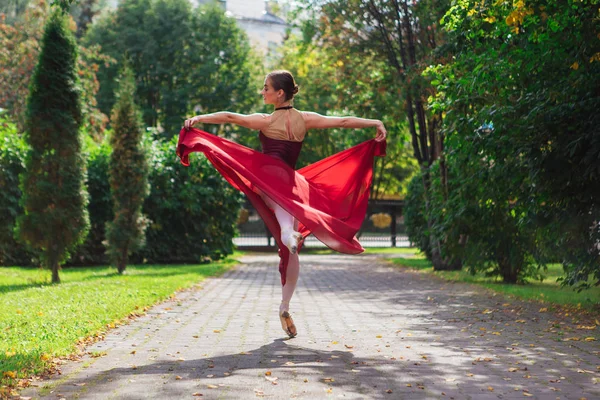 Mulher bailarina em vestido de balé vermelho dançando em sapatos pointe no parque de outono . — Fotografia de Stock
