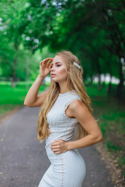 Portret van een charmante blonde vrouw met mooie witte jurk op de weg onder de bomen. — Stockfoto