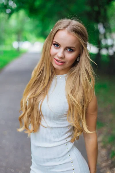 Retrato de una encantadora mujer rubia con hermoso vestido blanco de pie en la carretera bajo los árboles . —  Fotos de Stock