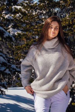 Kışın karlı dağ manzarasında mavi gözlü ve yüzünde çiller olan güzel esmer bir kadının portresi. Kışın güzel bir kız kürk ağacının yanında duruyor..