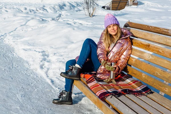 Menina loira bonita jovem senta-se em um banco no parque de inverno — Fotografia de Stock