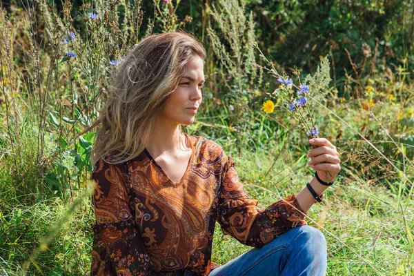 Ritratto di una bella donna felice, seduta sull'erba e con un fiore in mano — Foto Stock