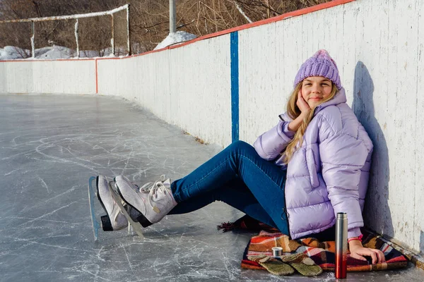 Krásná mladá žena relaxační po jízdě na bruslích a pití teplého nápoje z termo hrnce na kluzišti. — Stock fotografie