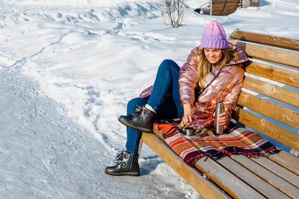 Menina loira bonita jovem senta-se em um banco no parque de inverno — Fotografia de Stock