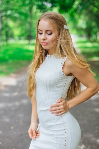 Retrato de una encantadora mujer rubia con hermoso vestido blanco de pie en la carretera bajo los árboles . —  Fotos de Stock