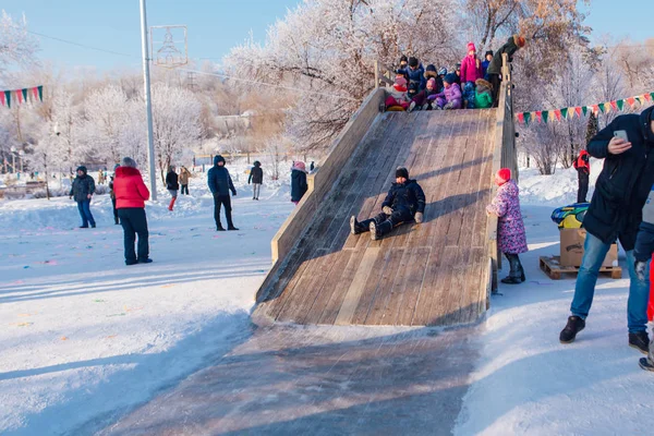 Novokuznetsk, russland - 07. Januar 2019: Russische Winterunterhaltung: Kinder beim Rodeln von der Holzrodelbahn — Stockfoto