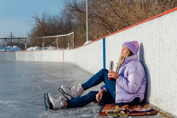 Belle jeune femme relaxante après avoir chevauché des patins à glace et bu une boisson chaude du termo pot sur la patinoire . — Photo