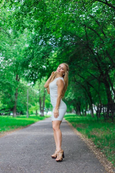 Portret van een charmante blonde vrouw met mooie witte jurk op de weg onder de bomen. — Stockfoto