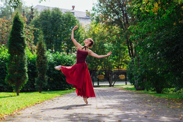 Ballerina donna in abito da balletto rosso che balla in scarpe da punta nel parco autunnale . — Foto Stock