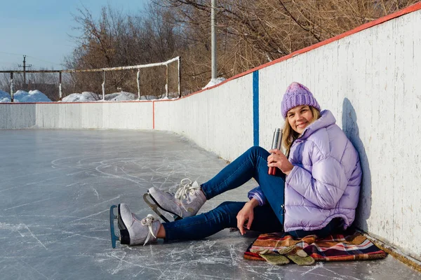 Прекрасна молода жінка розслабляється після катання на ковзанах і пиття гарячого напою з термоящика на ковзанці . — стокове фото