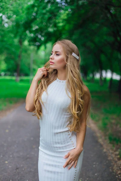 Egy bájos szőke nő portréja, gyönyörű fehér ruhában, ahogy a fák alatt áll az úton.. — Stock Fotó