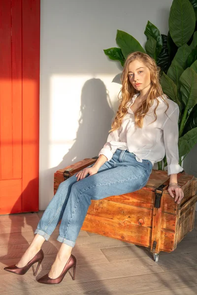 Joven hermosa mujer sentada en la caja de madera junto a la planta verde — Foto de Stock