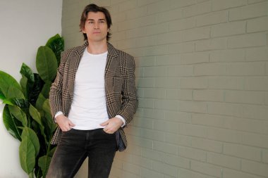 Gri duvarın yanında duran uzun boylu yakışıklı adam.