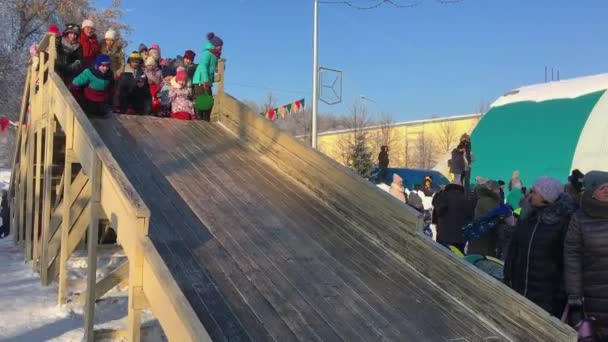 Novokuznetsk, Russia- January 07, 2019: Russian winter entertainment: children having fun tobogganing from wooden toboggan — Stockvideo